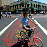 an asian woman on a bike rolling through a decorative crosswalk in chinatown/Oakland