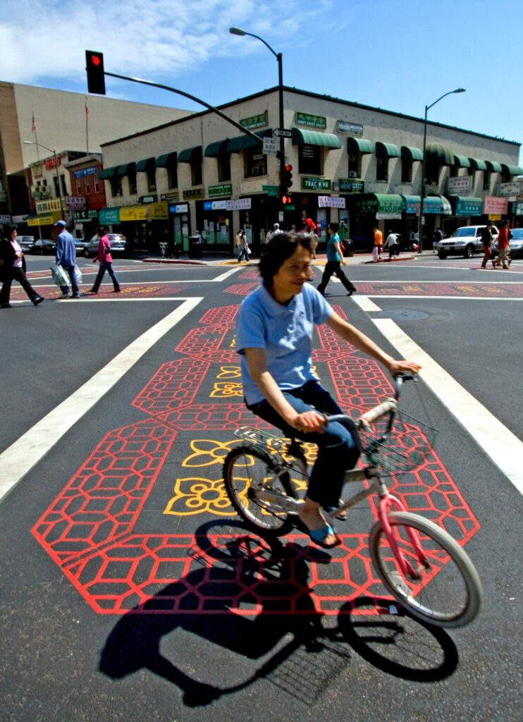 an asian woman on a bike rolling through a decorative crosswalk in chinatown/Oakland
