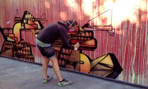 Image of an artist painting a mural on the Red Wall surrounding the Link Capitol Hill Station in Seattle, WA.