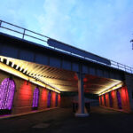 Image of over.under.pass in Greensboro, NC. The underpass is lit with red, purple, and white lights creating a friendly environment for people walking, rolling, or using the space.