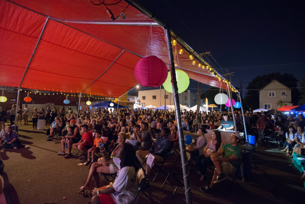 Image of Little Mekong Night Market. Large crowd sits underneath a red tent at night.