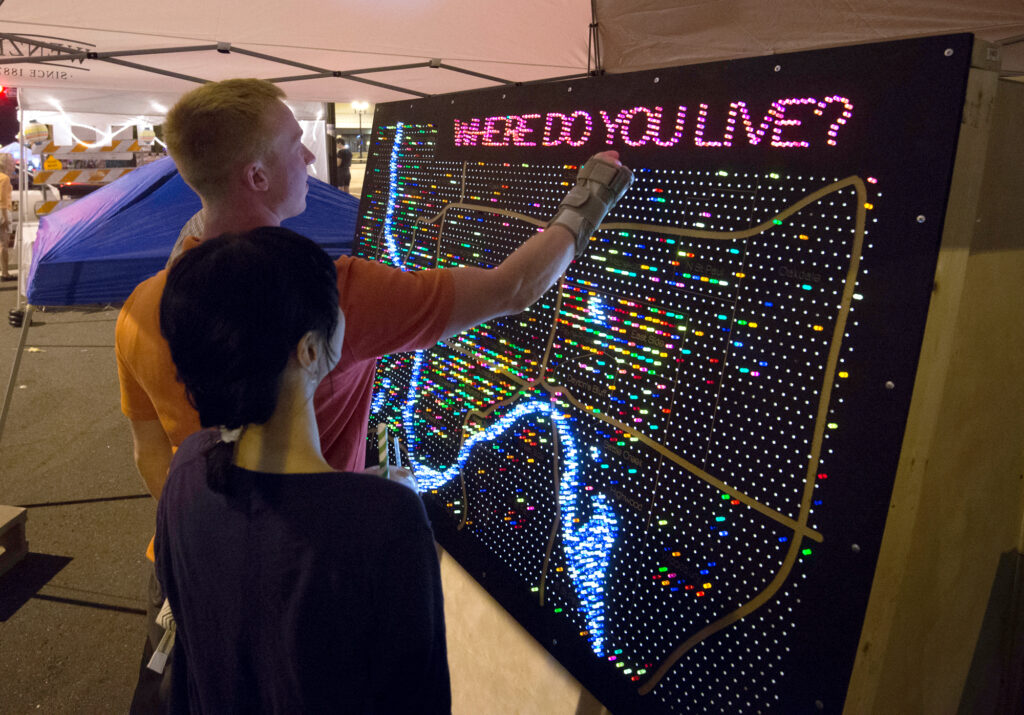 Image of Little Mekong Night Market. Two people engage with glowing neon map that reads "Where do you live?"