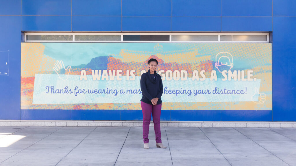 Artist in front of a creative banner at a transit station urging social distancing