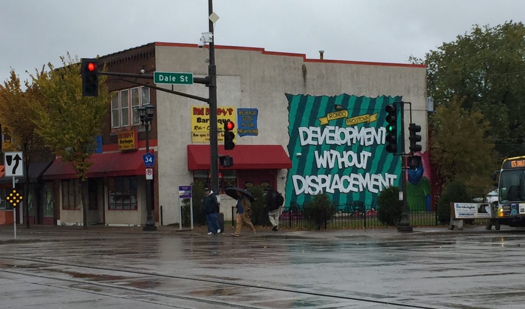 Image of street corner in the Rondo neighborhood of Saint Paul. On the side of the building is a mural that reads "Rondo Frogtown. Development without displacement."