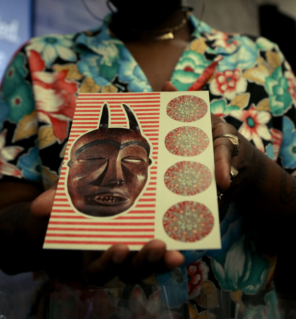 Image of a person holding a postcard with a red wooden cultural mask.