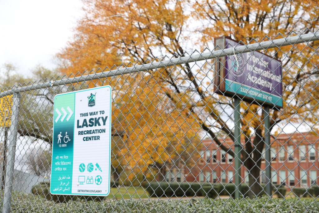 Image of teal and white sign attached to fence that features the Detroit logo and directs people to Lasky Recreation Center.