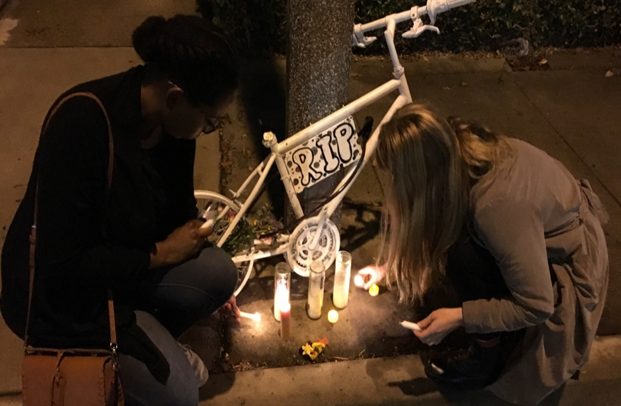 people lighting candles under a ghost bike memorial in LA
