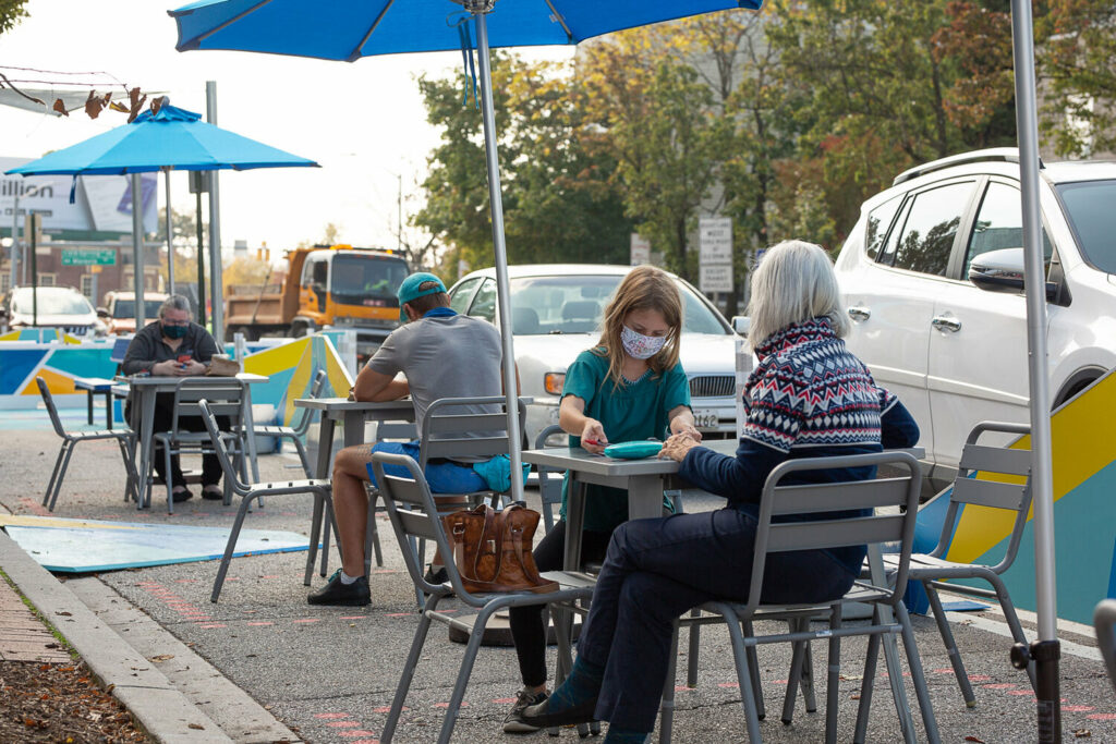 masked patrons dining at a sidewalk table installed in the street